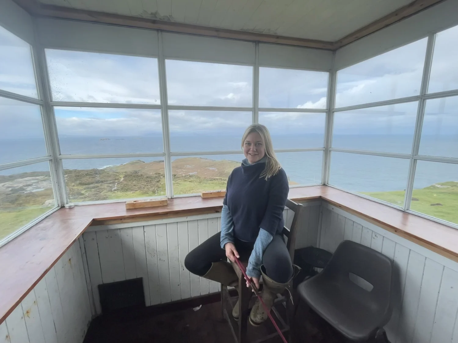 Emily seated in a windowed lookout overlooking the sea